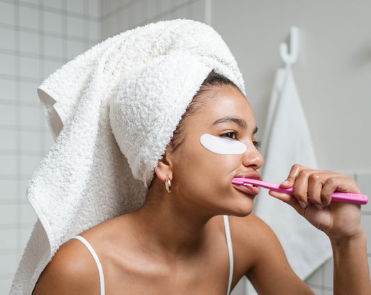 a woman with a towel wrapped around her head, brushing using an electric toothbrush