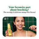 Smiling woman holding the Mango Bite Inspired Toothpaste and a loaded toothbrush
